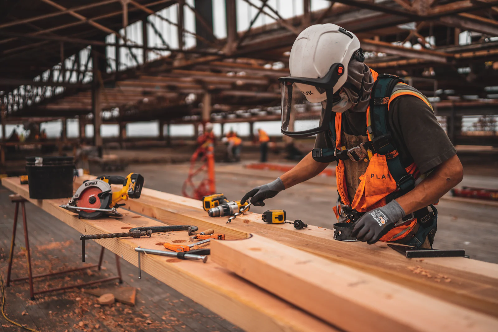 Construction worker in a safety helmet and harness measuring timber on site